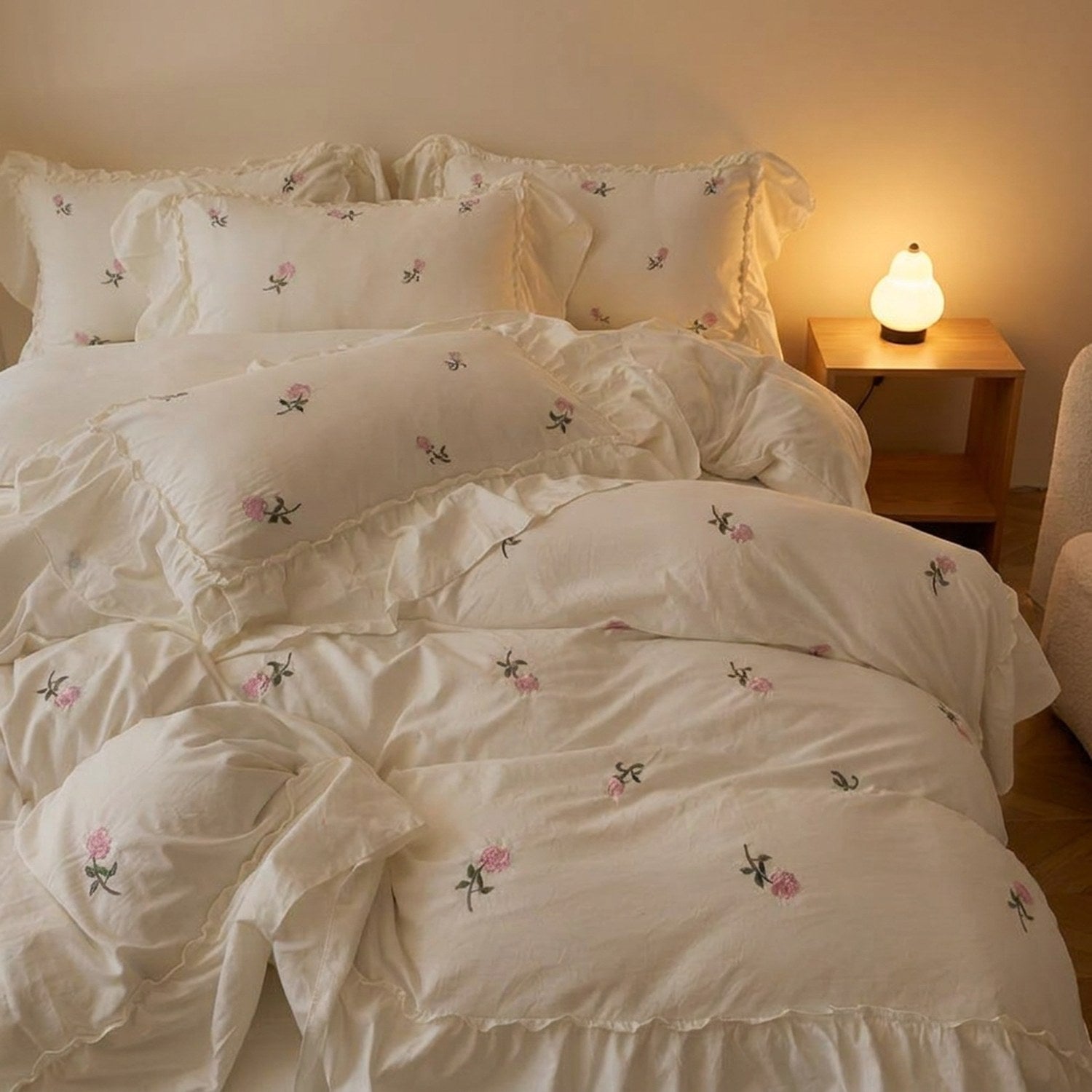 Parure de lit brodée de roses dans une chambre romantique avec table de chevet éclairée