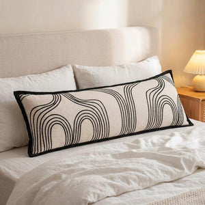 Traversin à motif arches noires posé sur un lit avec linge blanc et lampe de chevet
