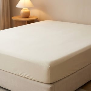 Drap housse beige sur un lit dans une chambre moderne avec table de chevet et lampe