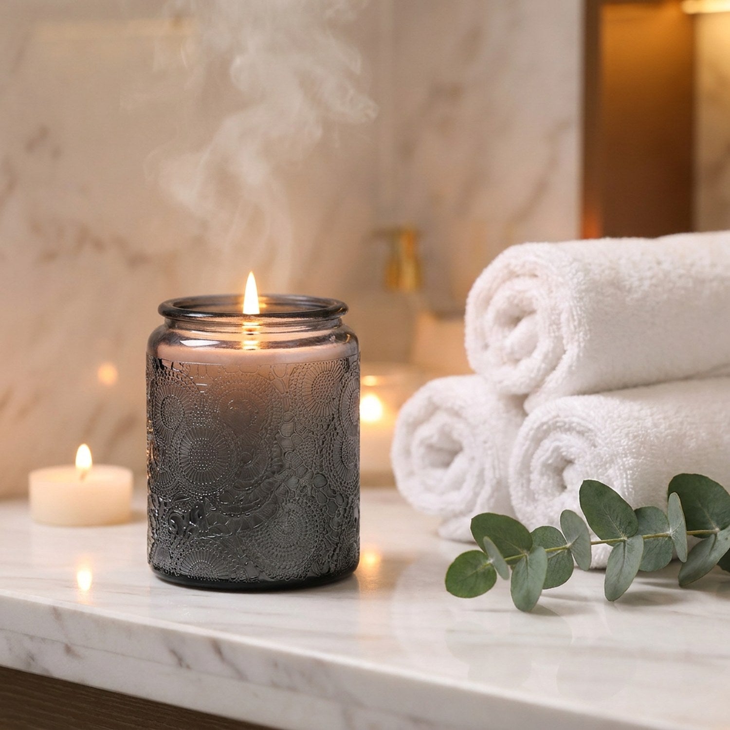 Bougie parfumée en verre gris sur marbre avec serviettes blanches et eucalyptus dans décor spa