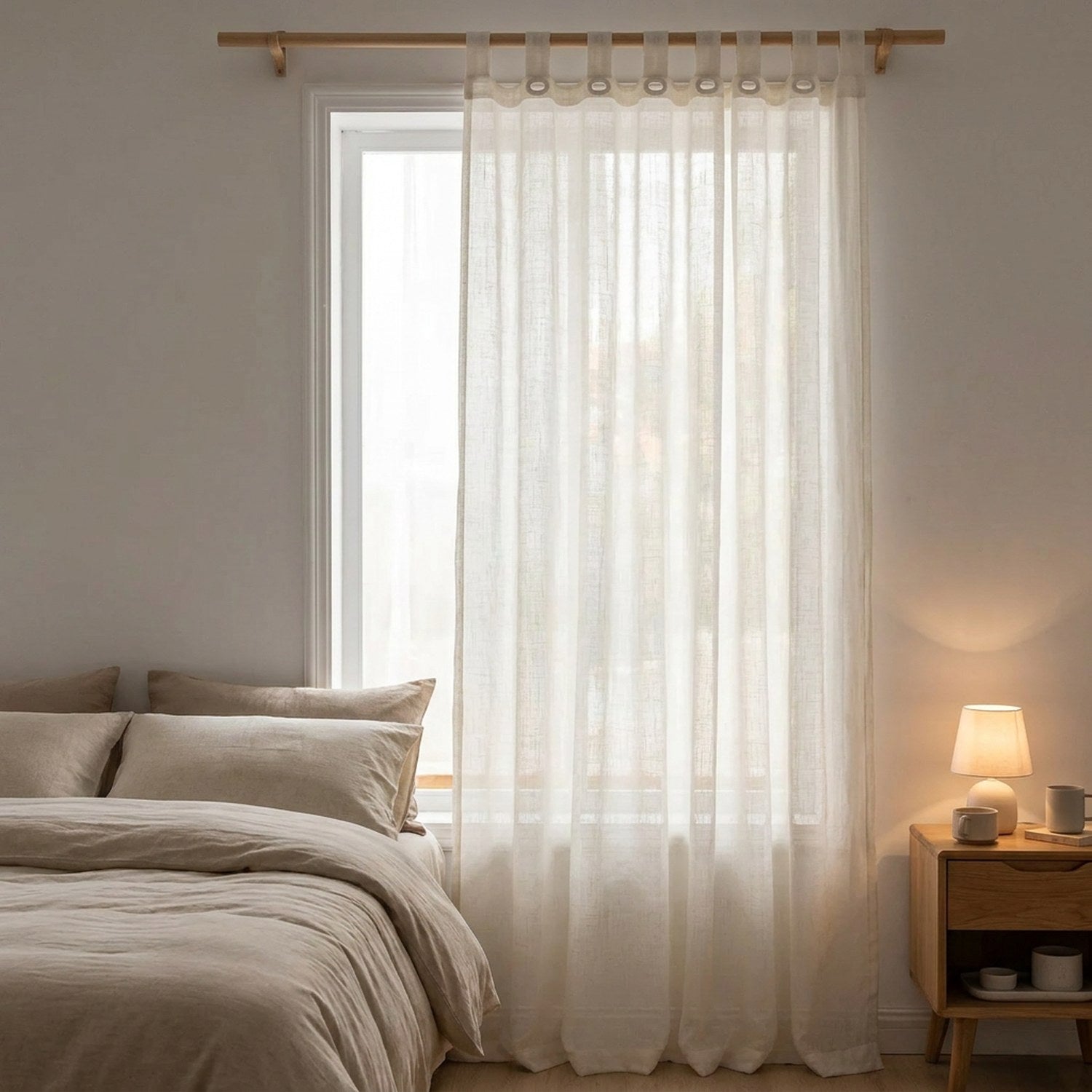 Voilage en lin blanc devant la fenêtre d'une chambre avec lit fait et table de chevet en bois