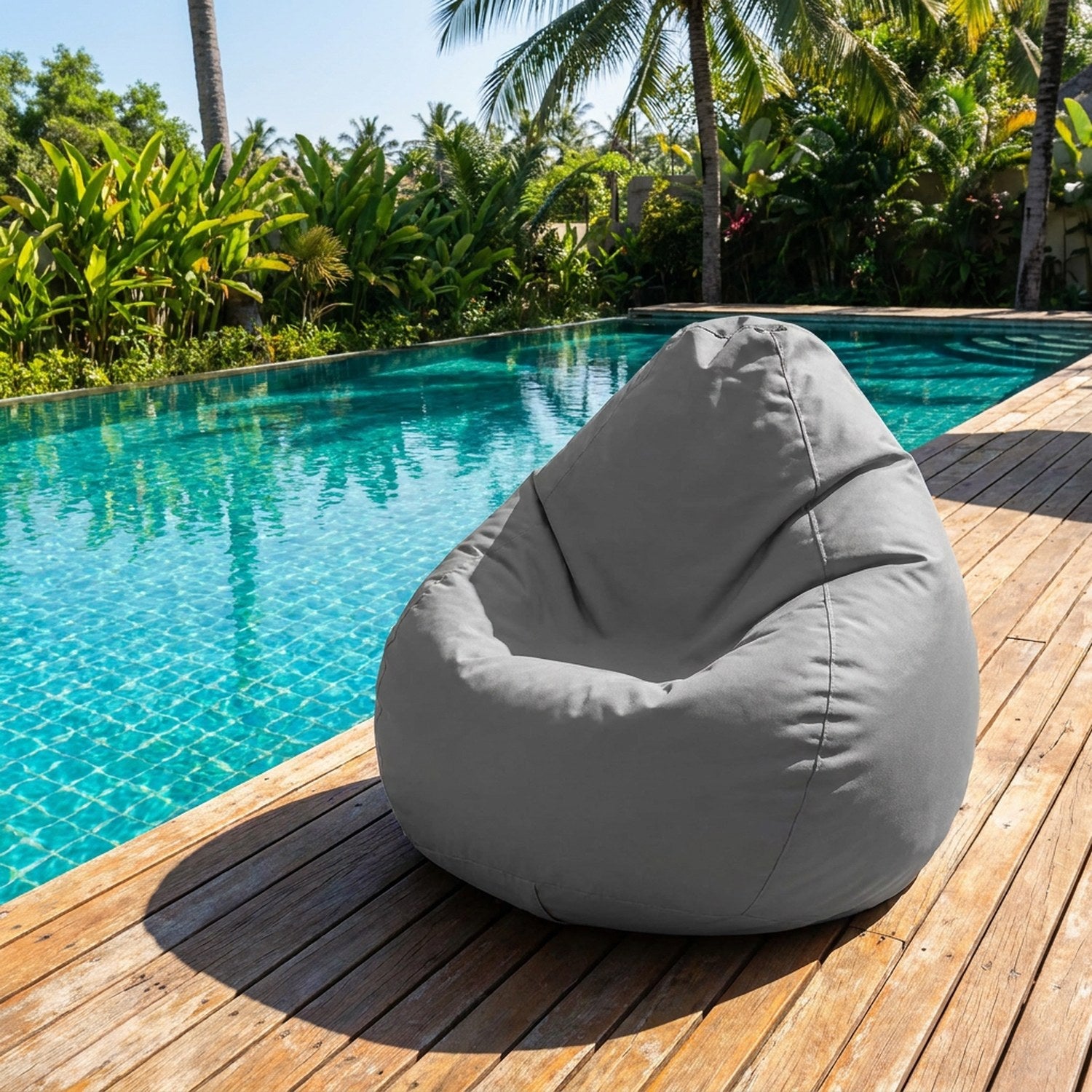 Housse de pouf poire grise posée sur une terrasse en bois au bord d'une piscine turquoise