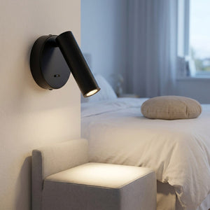 Applique murale ronde noire installée dans une chambre d'amis lumineuse avec banquette et coussin rond