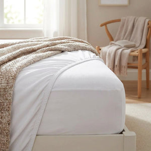 Coin de matelas avec housse blanche dans une chambre cosy et chaise en bois