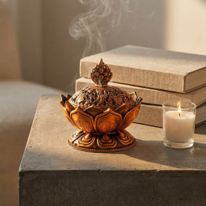 Porte-encens Bouddha bronze sur table béton en lumière golden hour avec bougie et livres