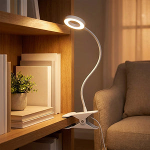 Lampe de bureau à pince fixée à une étagère en bois près de livres et d'une plante