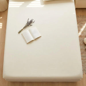 Vue du dessus d'un drap housse beige tendu avec un livre ouvert et des fleurs séchées