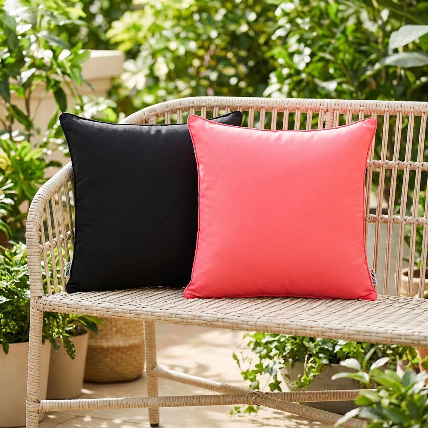 Housses de coussin extérieur noire et rose sur un banc de jardin entouré de verdure