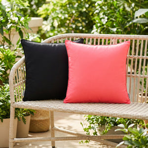 Housses de coussin extérieur noire et rose sur un banc de jardin entouré de verdure