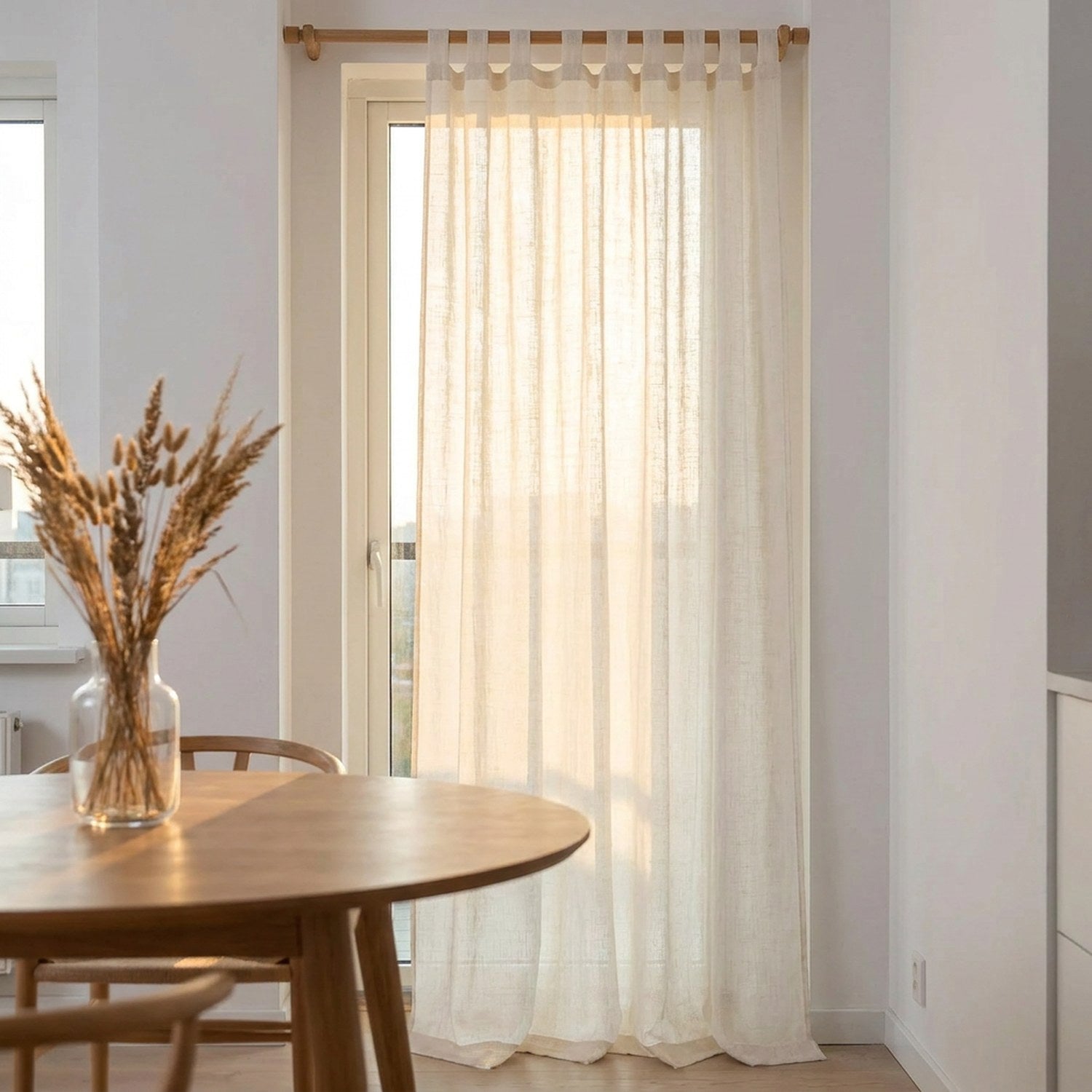 Voilage en lin blanc filtrant la lumière dorée près d'une table à manger ronde en bois