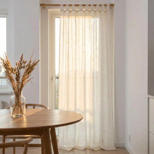 Voilage en lin blanc filtrant la lumière dorée près d'une table à manger ronde en bois