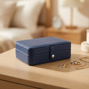 Boîte à bijoux en cuir bleu foncé fermée posée sur une commode avec des bagues