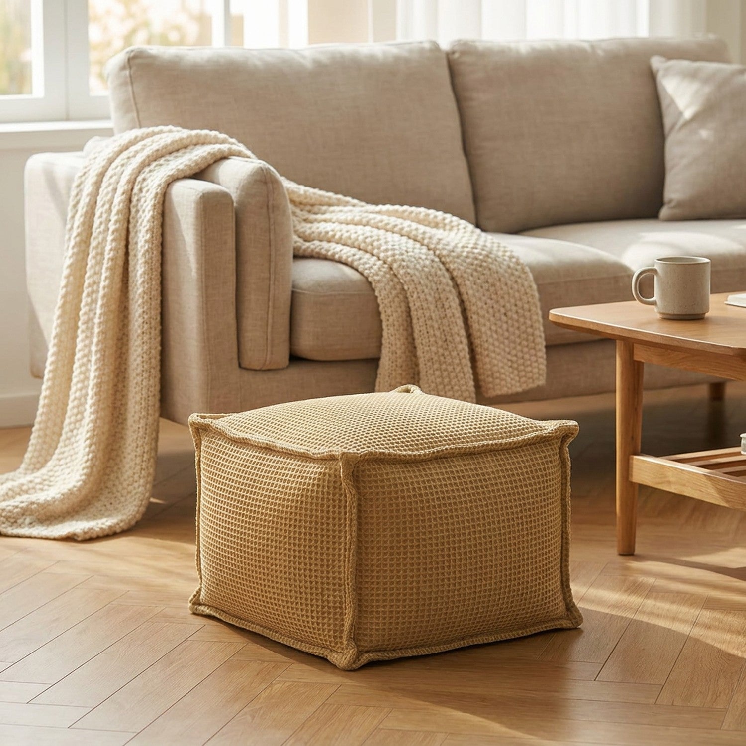 Pouf gaufré kaki utilisé comme repose-pieds au pied d'un canapé en lin