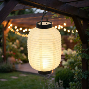 Lanterne japonaise en papier suspendue à une pergola de jardin avec guirlande lumineuse en soirée