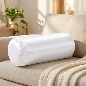 Traversin cylindrique satiné blanc posé sur un canapé en lin beige dans un salon lumineux