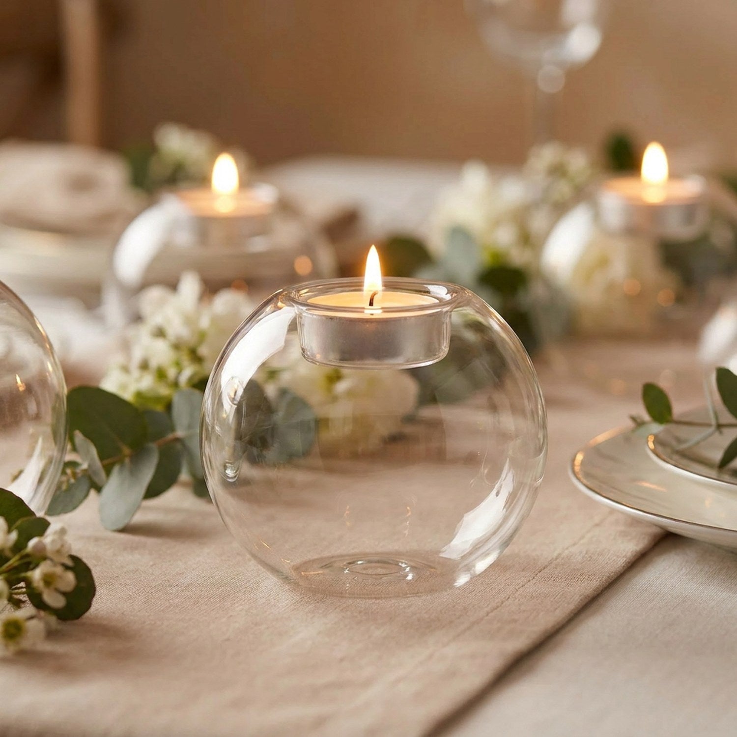 Bougeoir boule en verre allumé sur une table de mariage avec eucalyptus et fleurs blanches