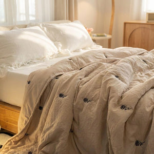 Couette d'été beige brodée de roses drapée sur un lit lumineux avec oreillers blancs