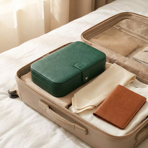 Boîte à bijoux voyage verte dans une valise ouverte sur lit blanc avec foulard
