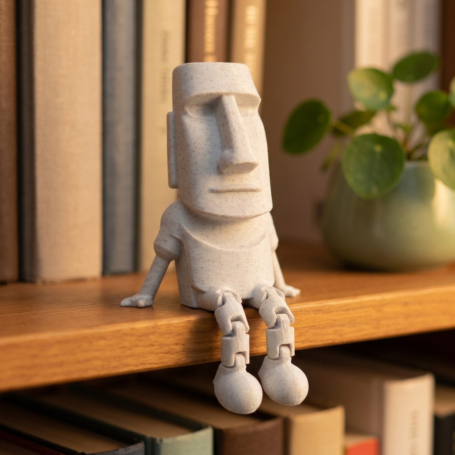 Statue Moai articulée assise sur une étagère décorée de livres et d'une plante verte