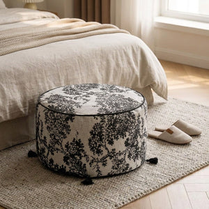 Pouf rond toile de Jouy au pied d'un lit dans une chambre chaleureuse
