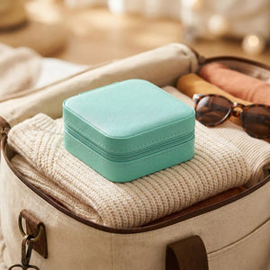 Boîte à bijoux turquoise fermée posée sur un sac de voyage