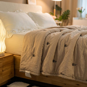 Couette d'été beige sur un lit avec table de chevet en bois et lampe chaleureuse