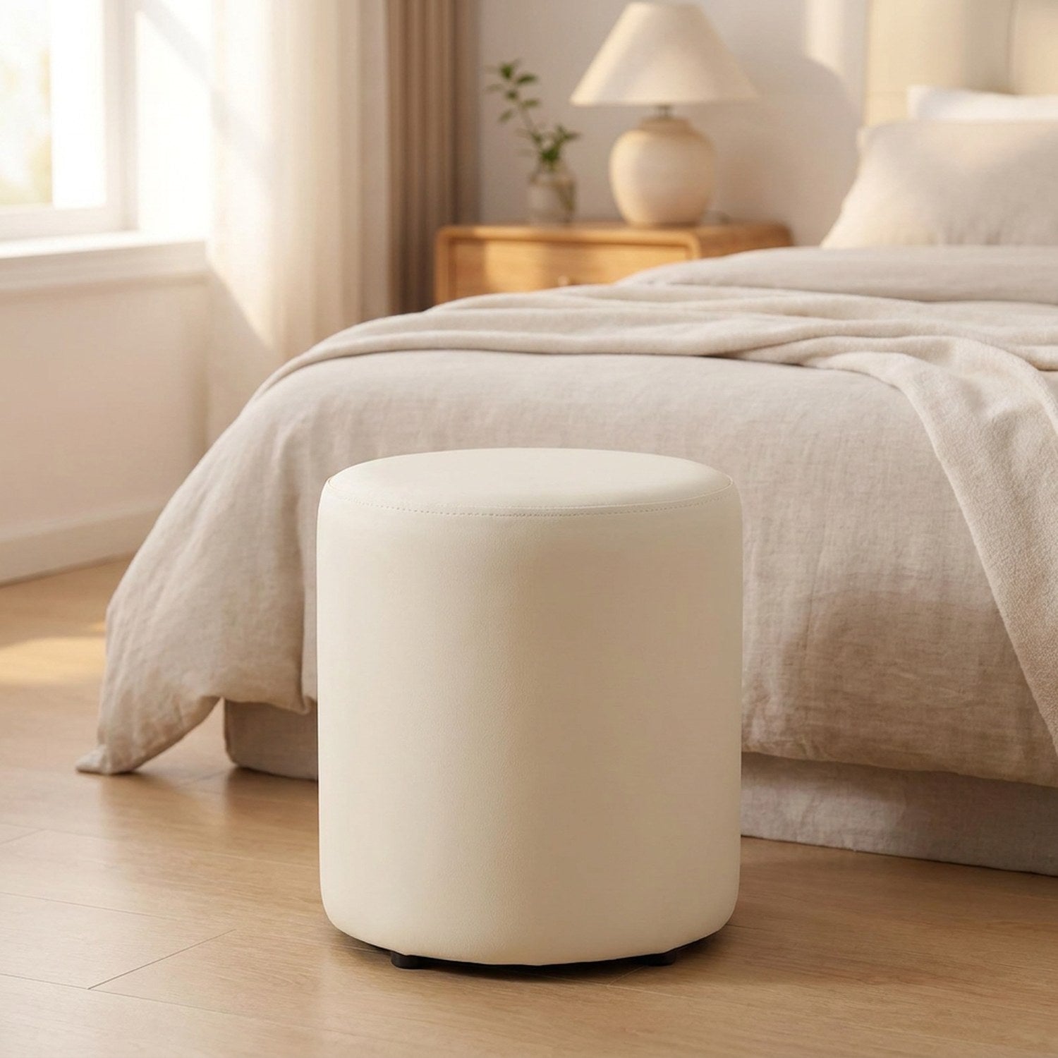 Tabouret pouf rond crème au pied d'un lit dans une chambre lumineuse