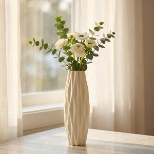 Vase origami blanc près d'une fenêtre avec des fleurs blanches et de l'eucalyptus