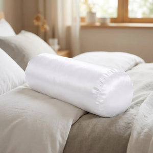Traversin cylindrique satiné blanc en gros plan sur un lit aux draps clairs