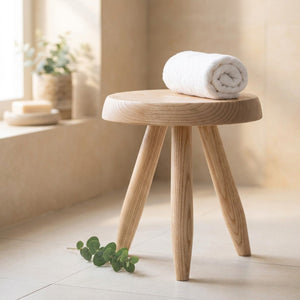 Tabouret rond en bois clair avec une serviette roulée dans une salle de bain lumineuse