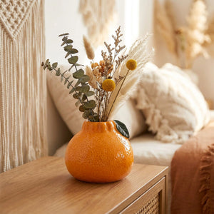 Vase orange en céramique avec un bouquet de fleurs séchées sur une table de chevet