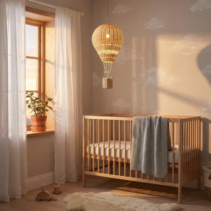 Chambre bébé scandinave avec lustre ballon rotin suspendu au-dessus du berceau bois naturel