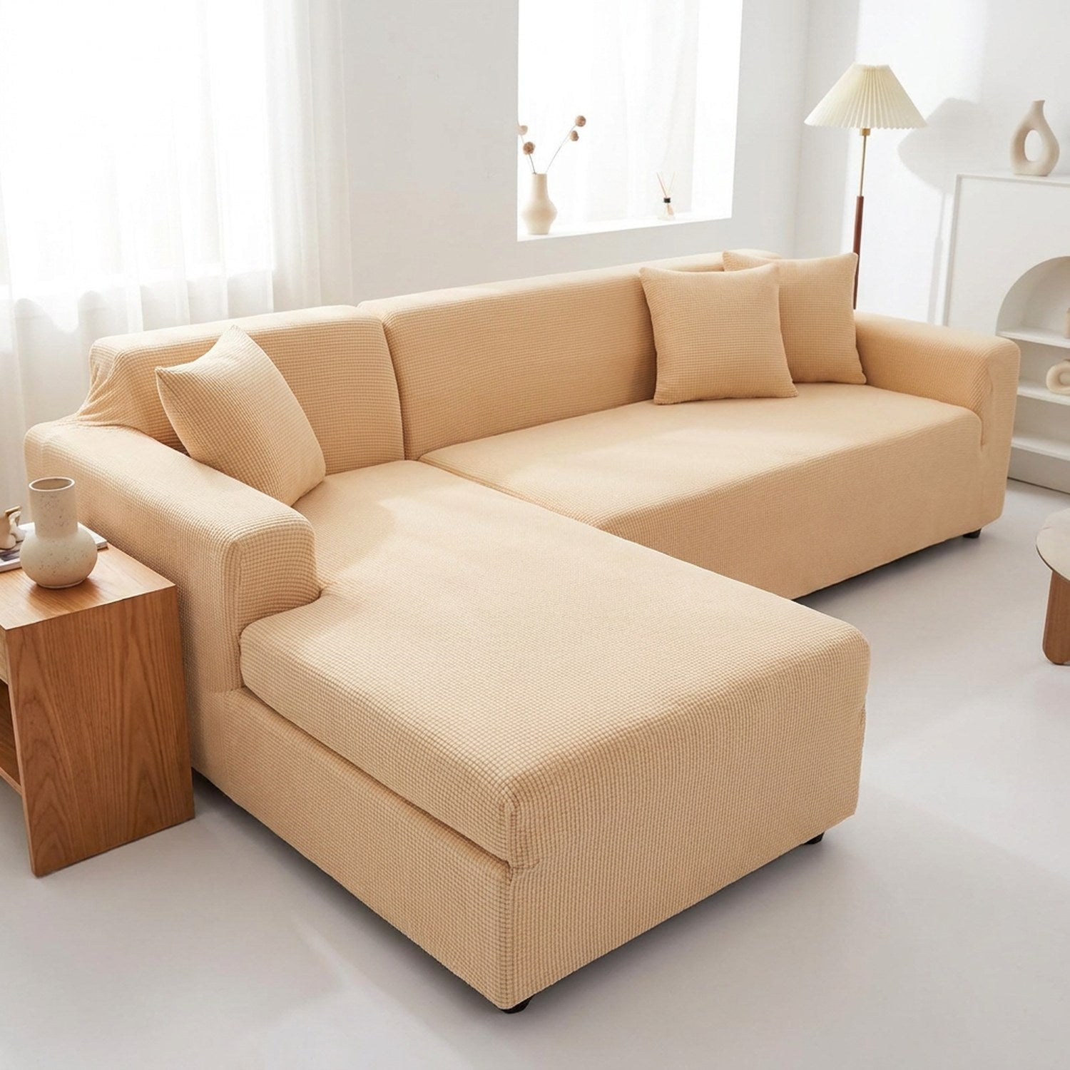 Housse de canapé extensible beige installée sur un canapé d'angle moderne dans un salon lumineux