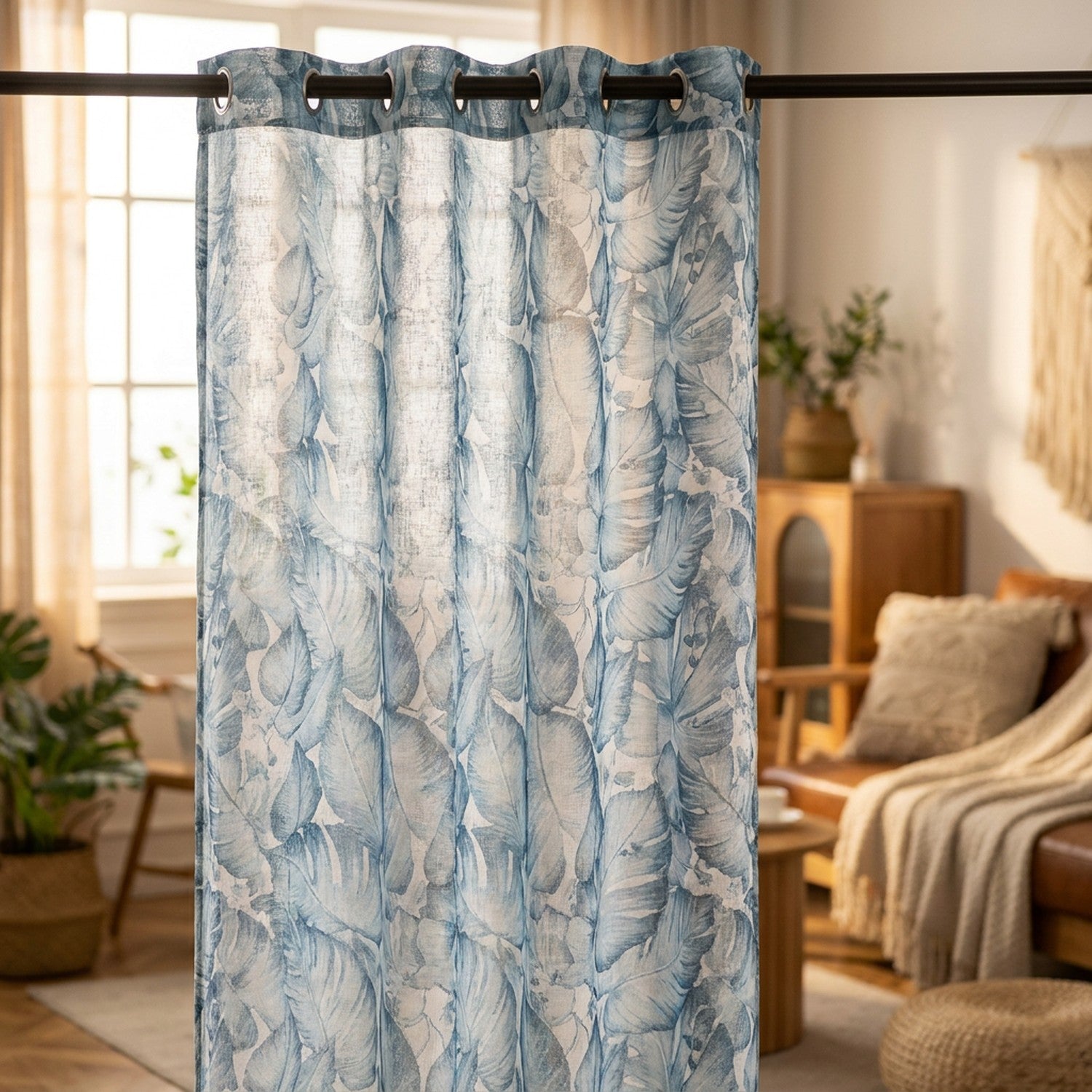 Rideau voilage bleu à motif feuillage tropical suspendu devant une fenêtre lumineuse