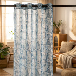 Rideau voilage bleu à motif feuillage tropical suspendu devant une fenêtre lumineuse