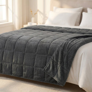Couverture lestée grise drapée sur un lit avec oreillers blancs dans une chambre chaleureuse et lumineuse