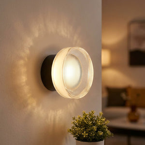 Applique murale LED ronde noire au verre strié diffusant une lumière chaude dans un salon