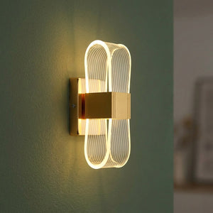 Applique murale dorée au design ruban lumineux infini diffusant une lumière chaude sur un mur moderne