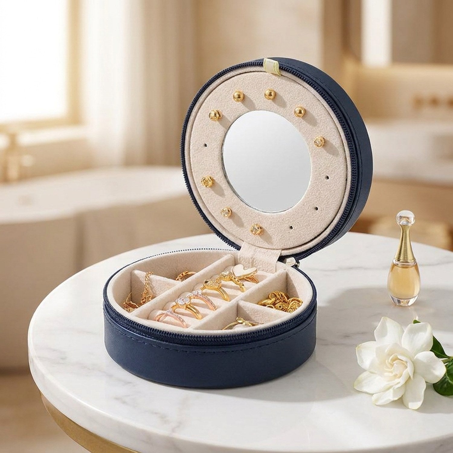 Coffret à bijoux de voyage rond bleu marine ouvert sur table en marbre avec miroir intégré et compartiments velours