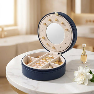 Coffret à bijoux de voyage rond bleu marine ouvert sur table en marbre avec miroir intégré et compartiments velours