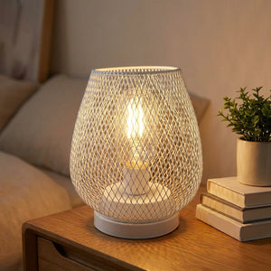 Lampe industrielle cage grillagée métal allumée sur une table de chevet