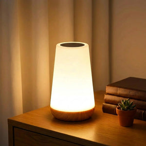 Lampe tactile RGB blanche et bois posée sur une table de chevet avec lumière chaude allumée