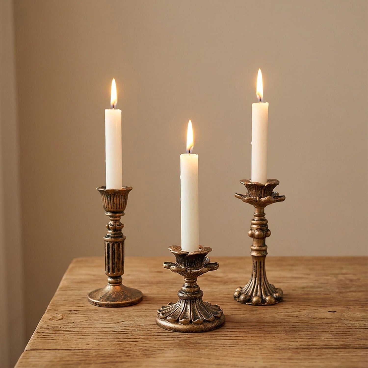 Bougeoirs vintage bronze antique en résine, 3 modèles avec bougies allumées sur table en bois