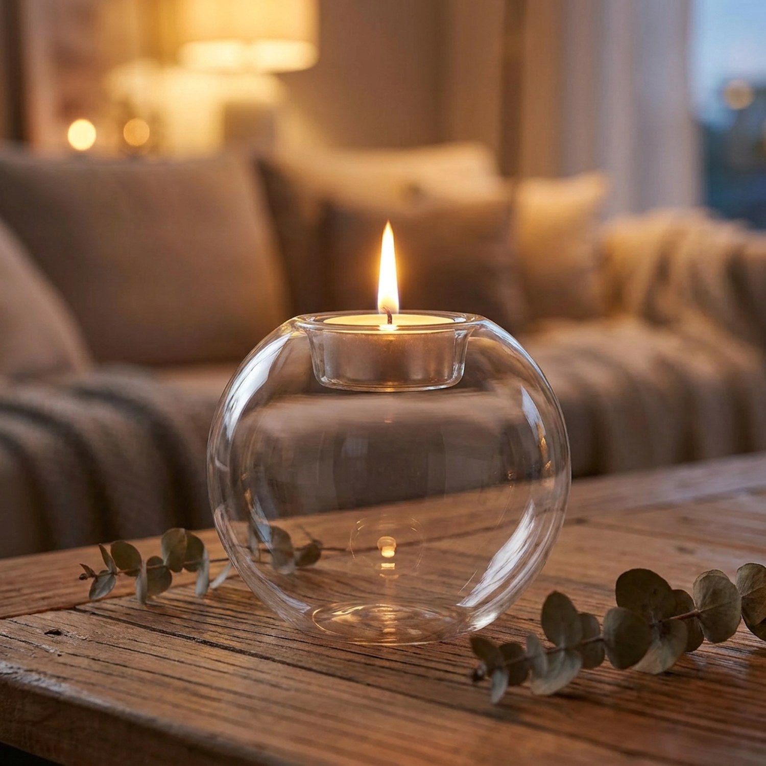 Bougeoir boule en verre transparent avec une bougie chauffe-plat allumée posé sur une table en bois
