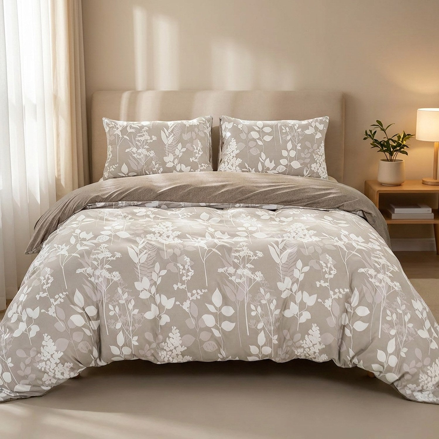 Parure de lit au feuillage blanc sur fond taupe installée sur un lit dans une chambre lumineuse et chaleureuse