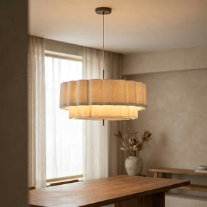 Suspension ronde en tissu beige plissé allumée au-dessus d'une table en bois dans un salon lumineux