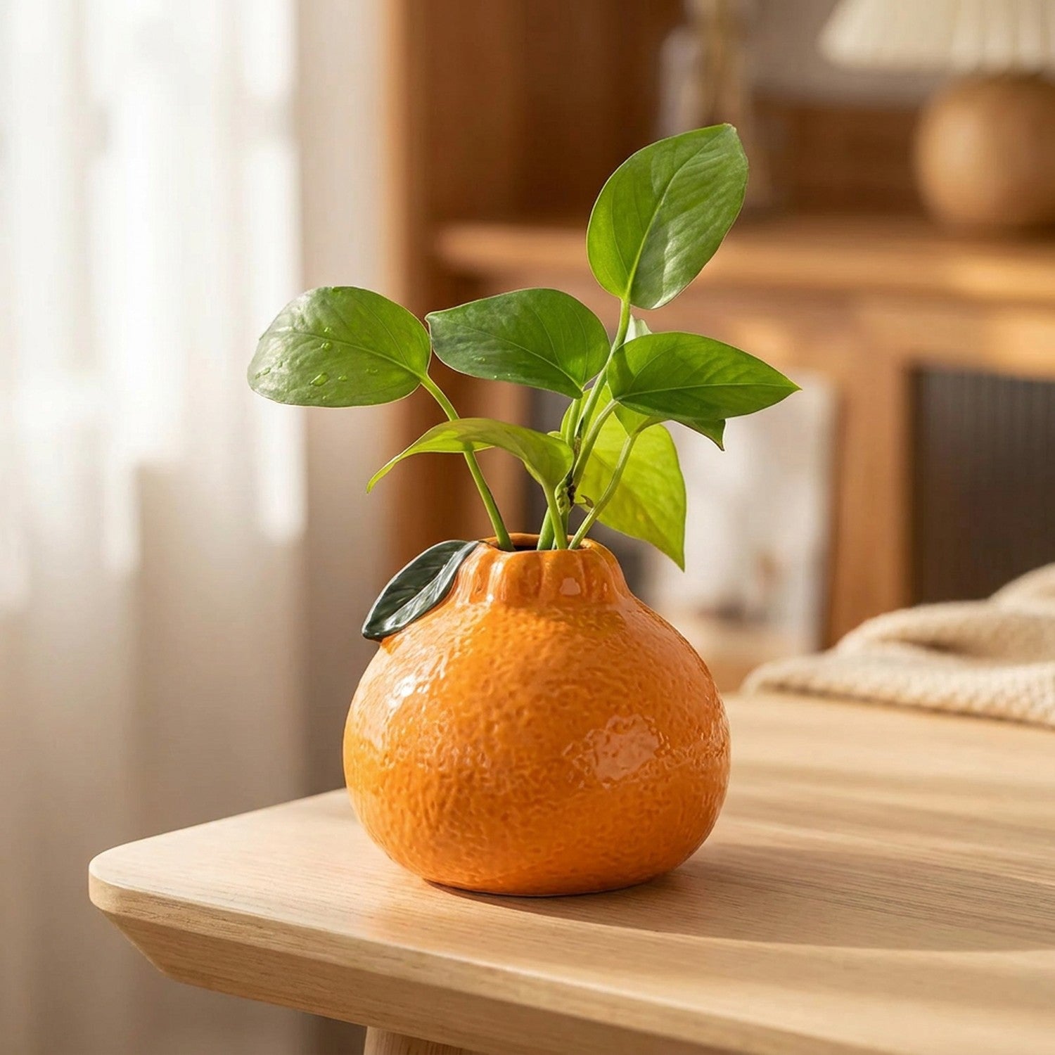 Vase original en céramique en forme d'orange avec une bouture verte sur une table en bois