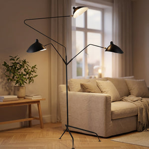 Lampadaire trépied en métal noir à trois bras articulés allumé dans un salon chaleureux