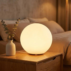 Lampe boule veilleuse allumée diffusant une lumière chaude posée sur une table de chevet en bois