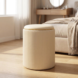 Tabouret de rangement rond beige à l'assise rembourrée et liseré doré posé dans une chambre lumineuse